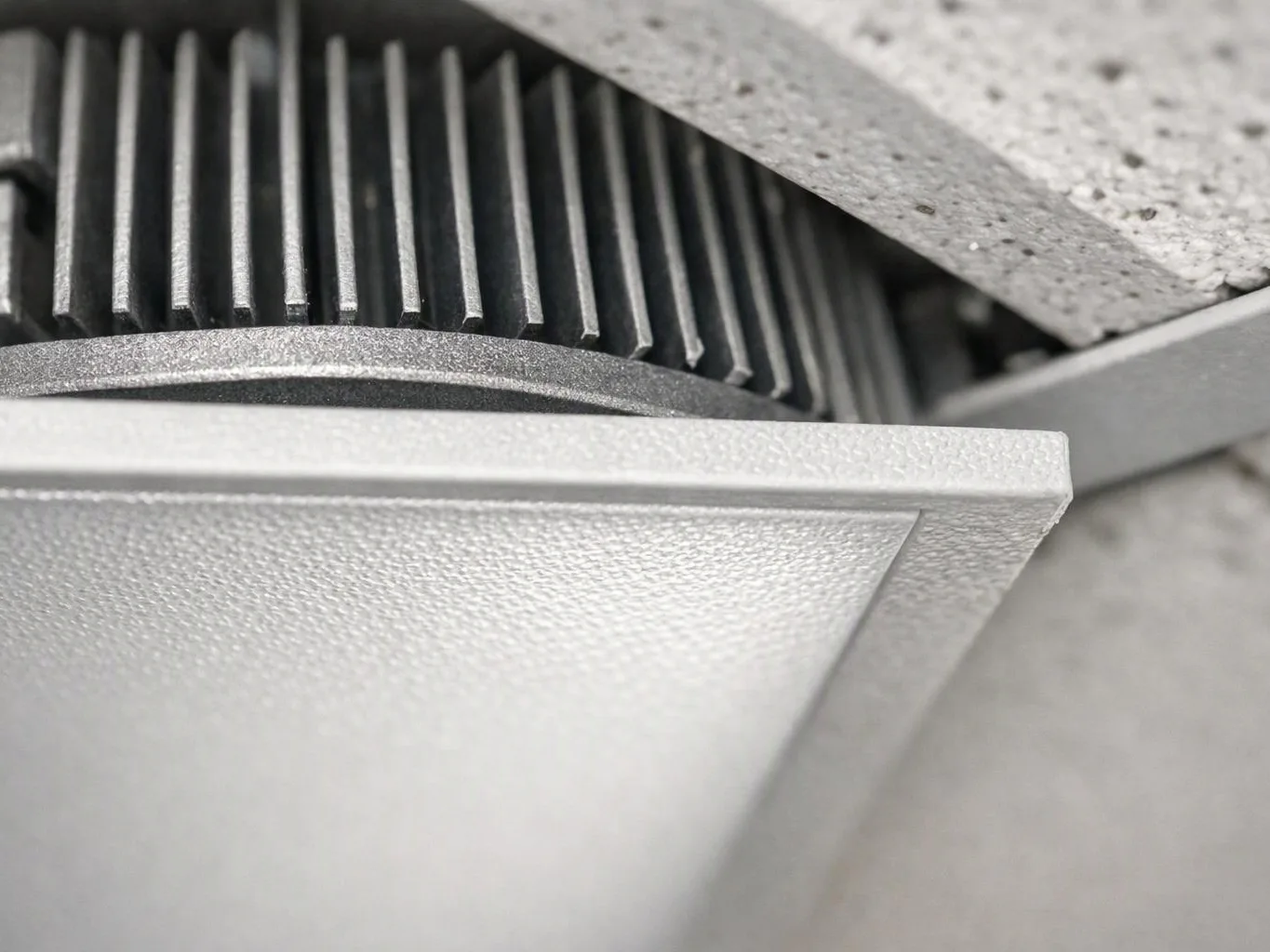 Close-up of a ceiling light fixture showing a textured white panel and dark metal fins