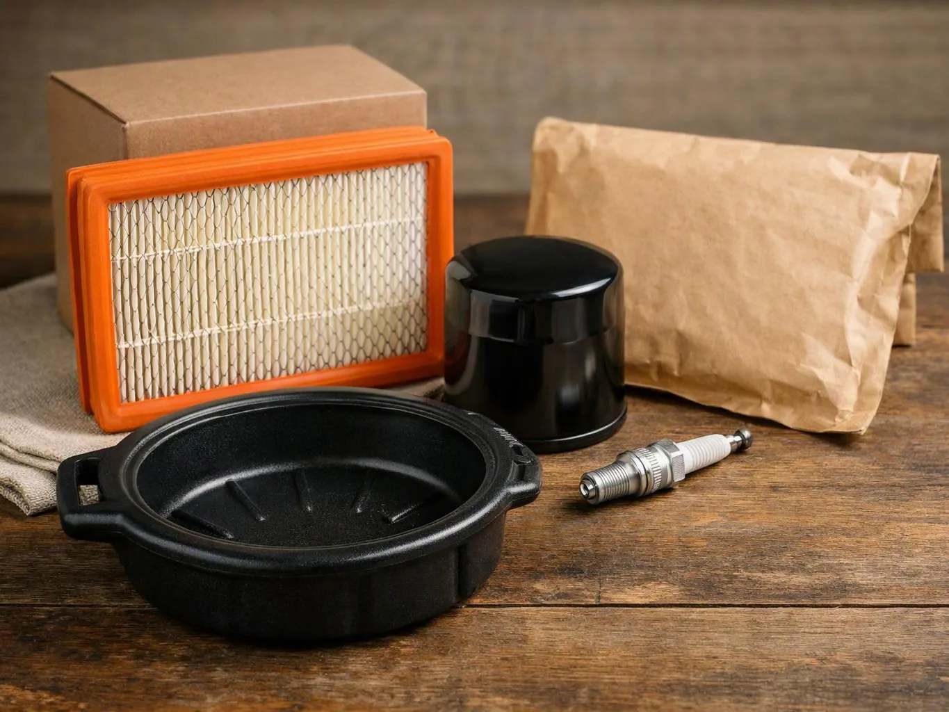 A group of car maintenance parts sits on a wooden table, including a filter, oil pan, spark plug, and wrapped package